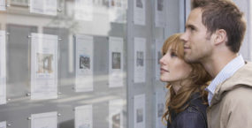 young-couple-looking-at-window-build-to-rent-communities-display-real-estate-office